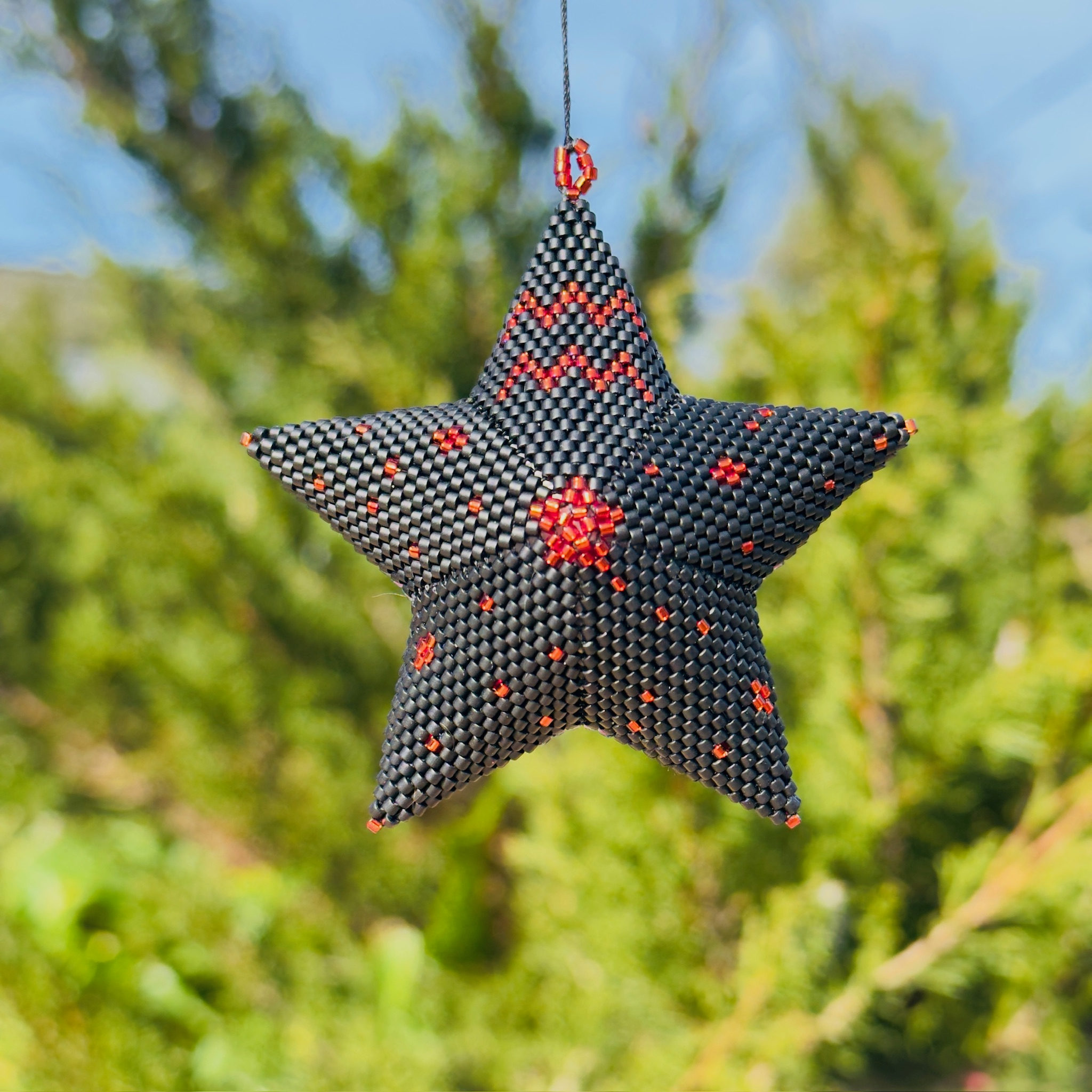 Beaded star ornament in dark charcoal with red accent beads hanging outdoors