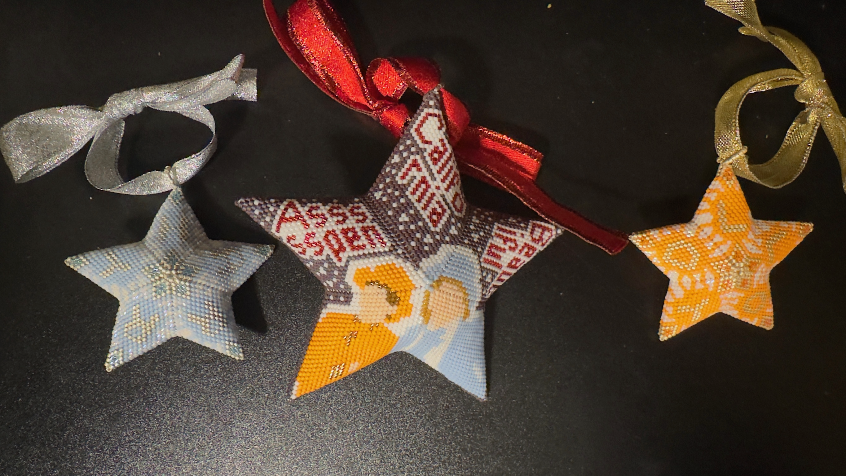 Three beaded star ornaments with ribbons featuring nativity and festive designs