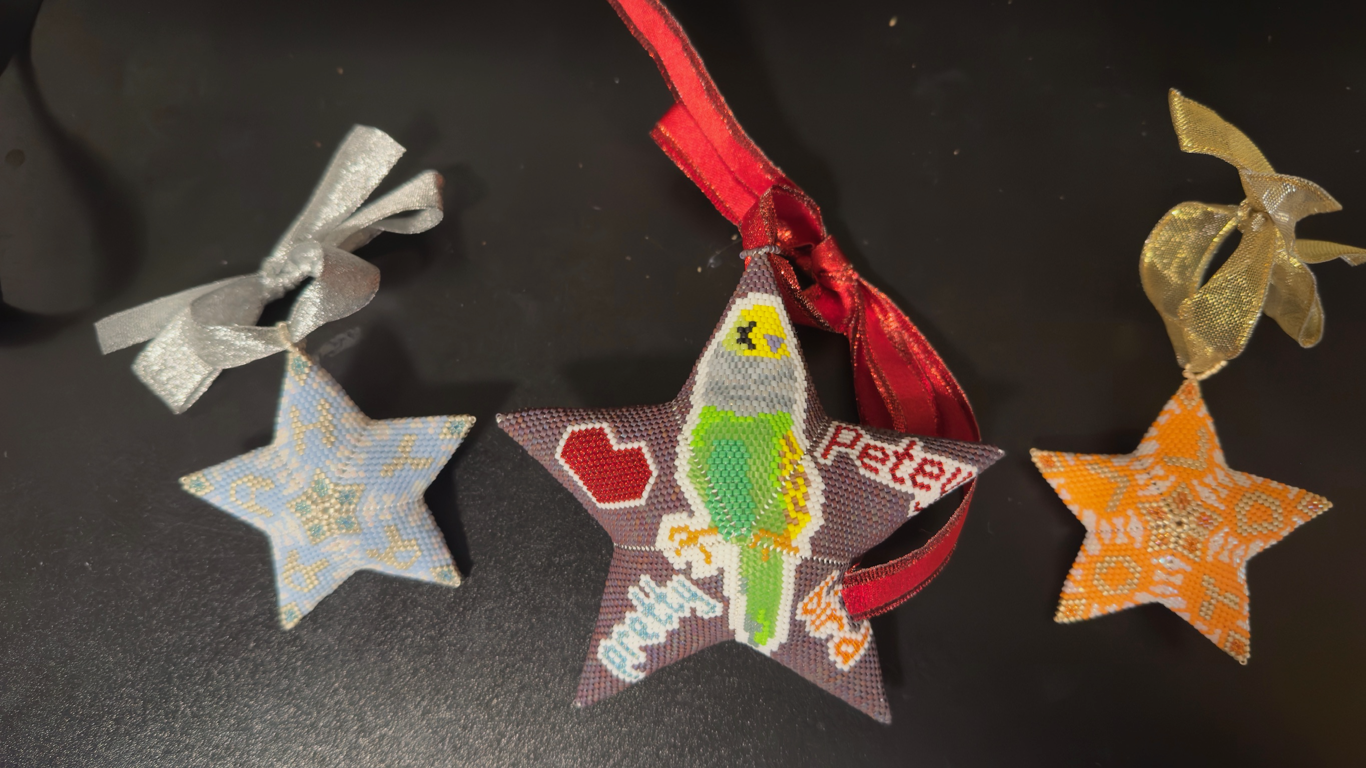 Three beaded star ornaments with ribbons featuring a parrot and colorful patterns